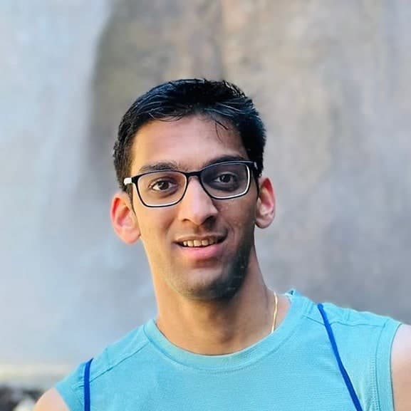 Ishaan Shete smiling, outdoors in front of a rock face